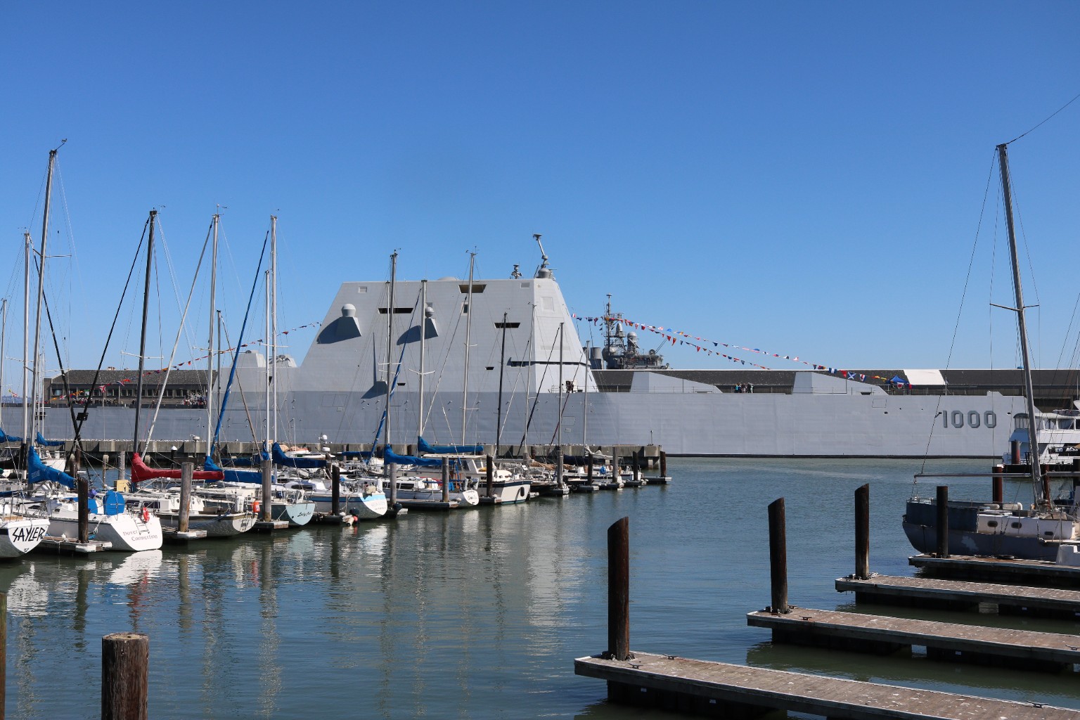USS Zumwalt DDG-1000 moored on the San Francisco waterfront behind a marina of sailboats